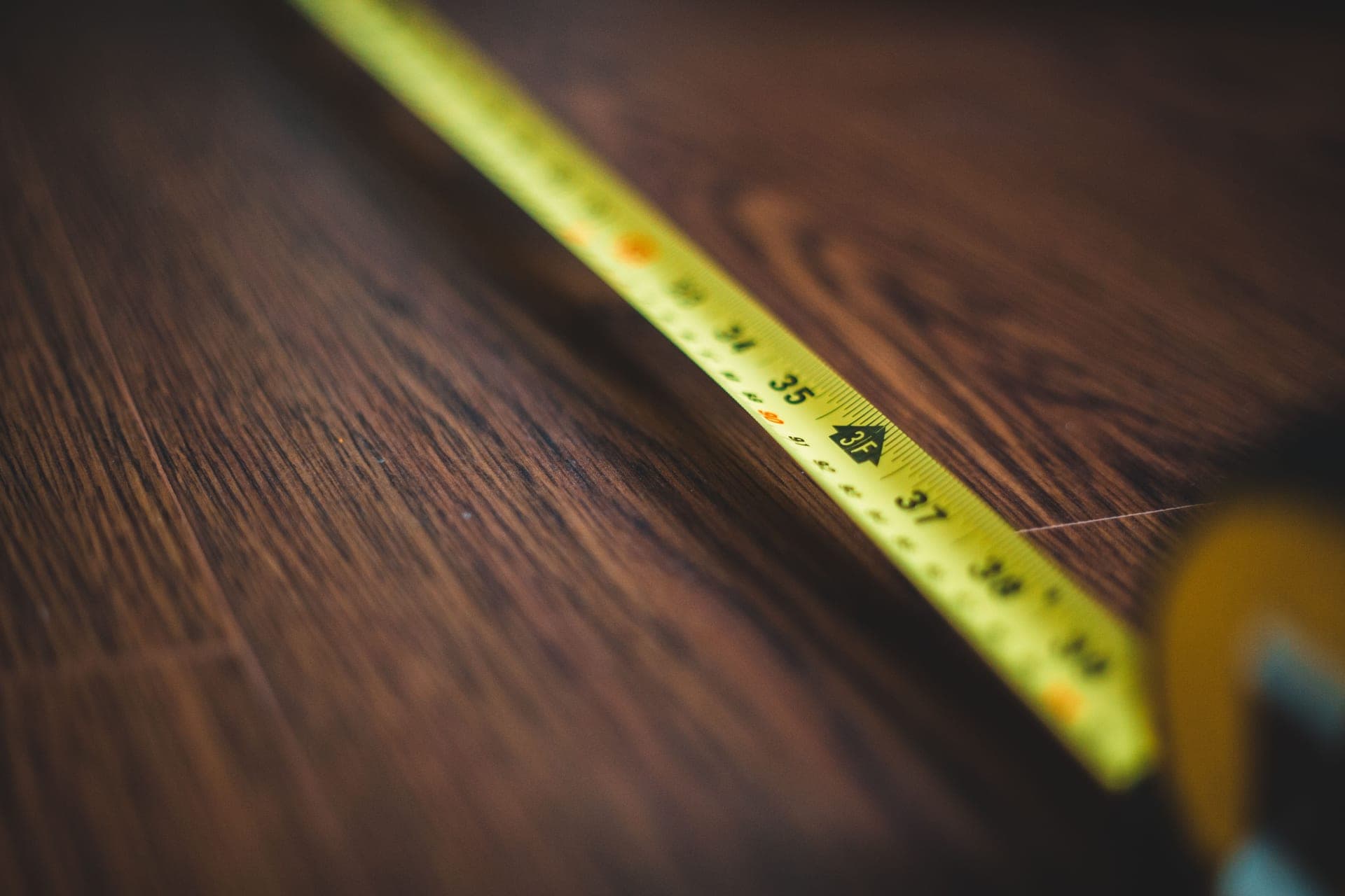 A tape measure laid across a wooden floor while a room is measured in daylight