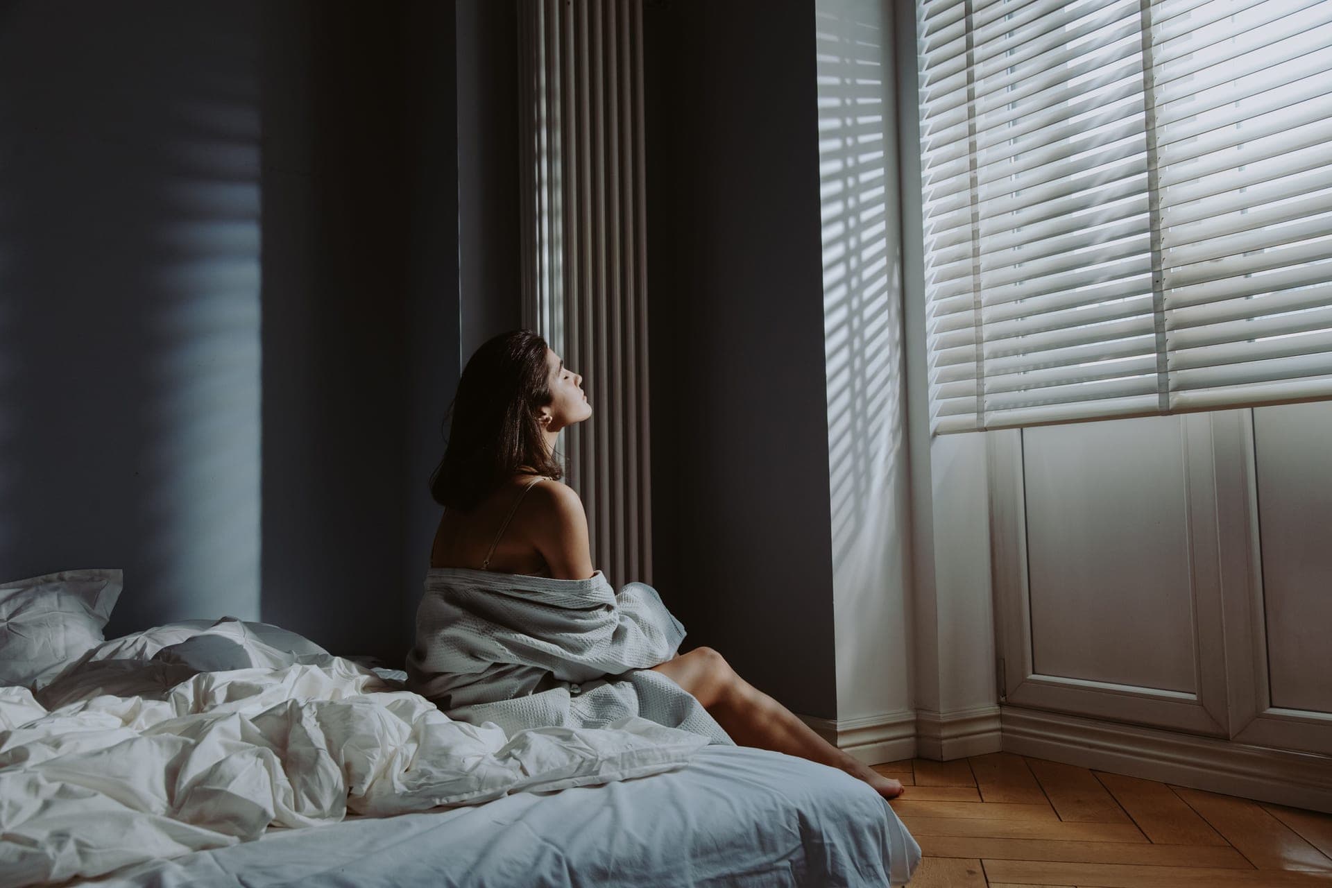 A bedroom with the blind drawn against late afternoon sun and a fan running at the foot of the bed